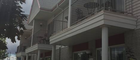 Un edificio de varios pisos con balcones, fachada de ladrillo y un camino pavimentado con plantas.