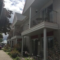 A multi-story building with balconies, a brick facade, and a paved walkway with plants.