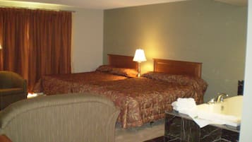 Habitación de hotel con cama, una silla, una mesita de noche con lámpara, y un baño con lavamanos y espejo.