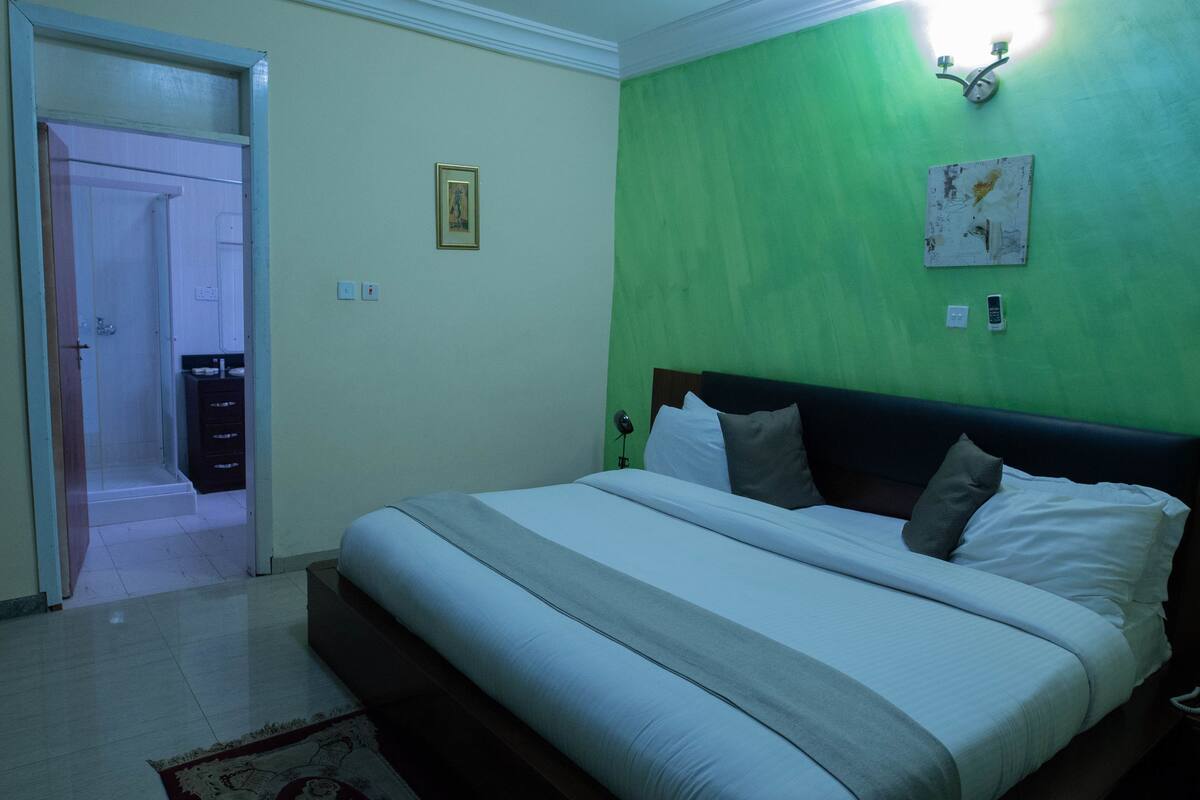Quarto com cama, mesa de cabeceira, luminária na parede e parede verde.