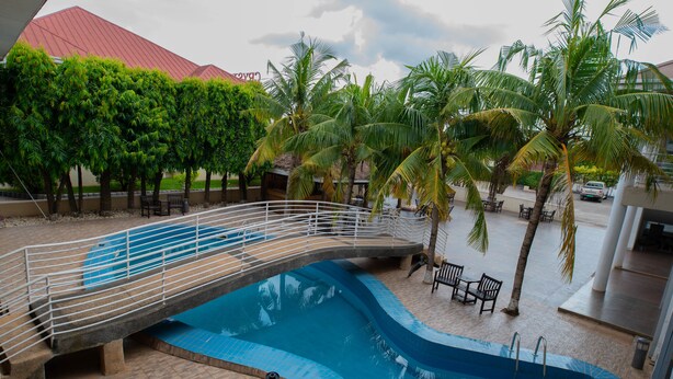 Una piscina con un puente, palmeras y asientos al aire libre.
