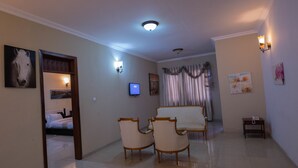Una habitación de hotel con una cama, televisión, dos sillones, una mesita y un teléfono.
