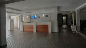 Zona de recepción de hotel con un mostrador, un televisor y una planta en maceta.