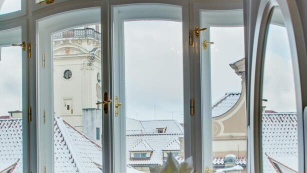 Una habitació amb un finestral gran, un armari blanc, un mirall i un ram de flors en un vas.