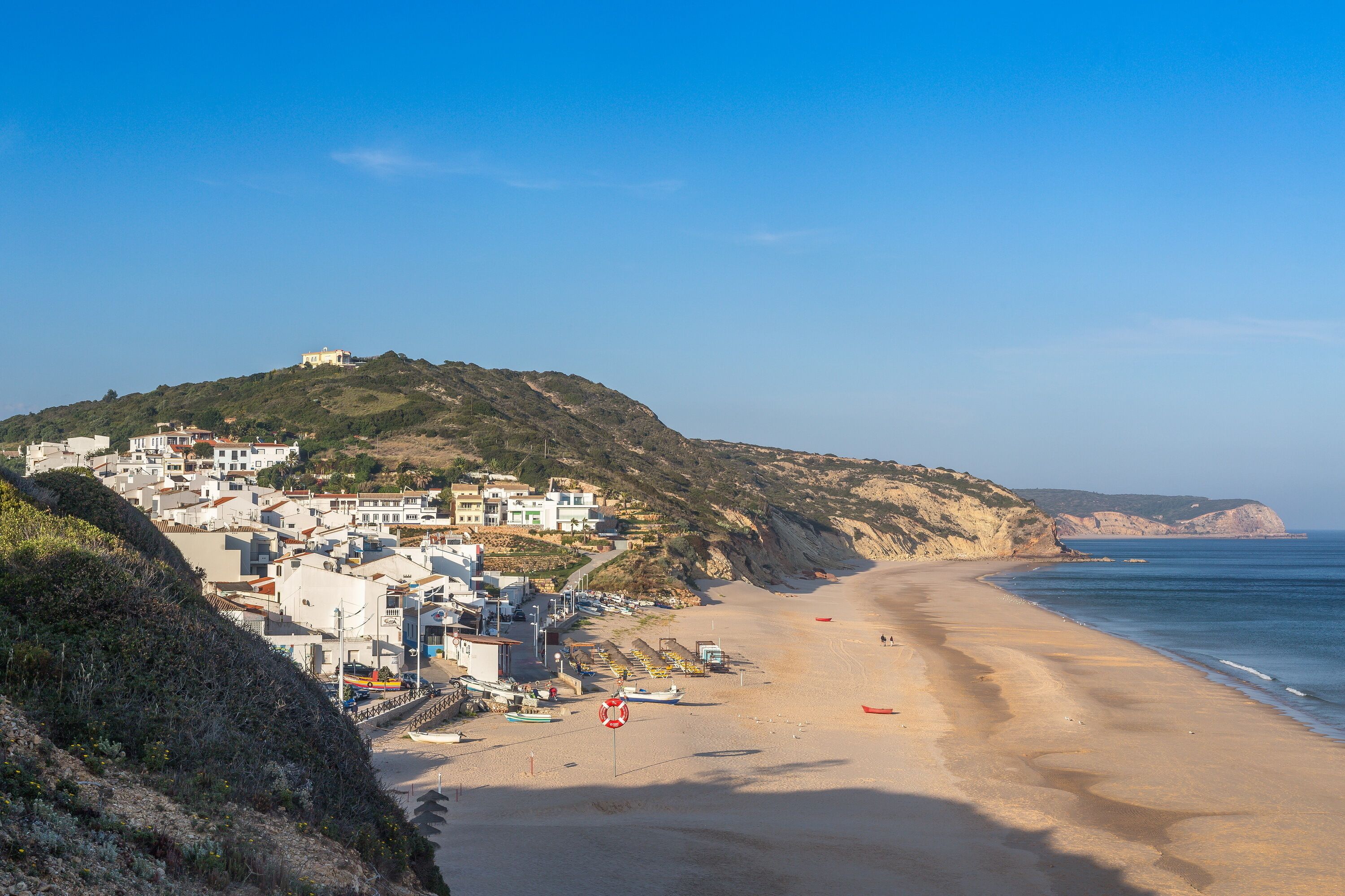 Un pueblo costero con edificios en una colina, una playa de arena y el mar.