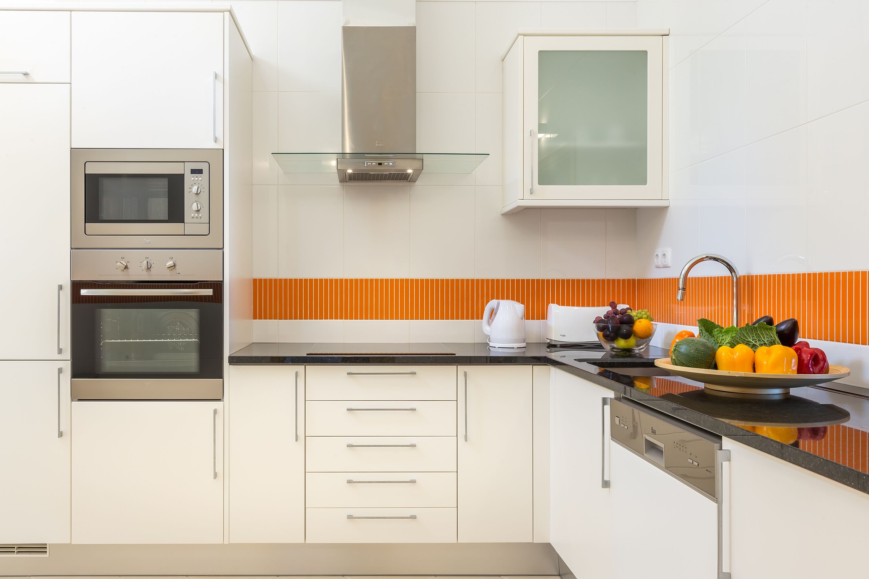 A modern kitchen with stainless steel appliances, white cabinetry, and a fruit bowl on the counter.