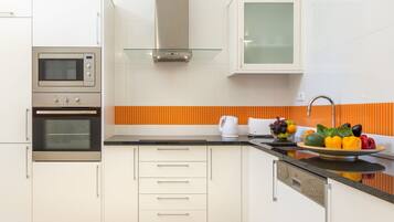 A modern kitchen with stainless steel appliances, white cabinetry, and a fruit bowl on the counter.