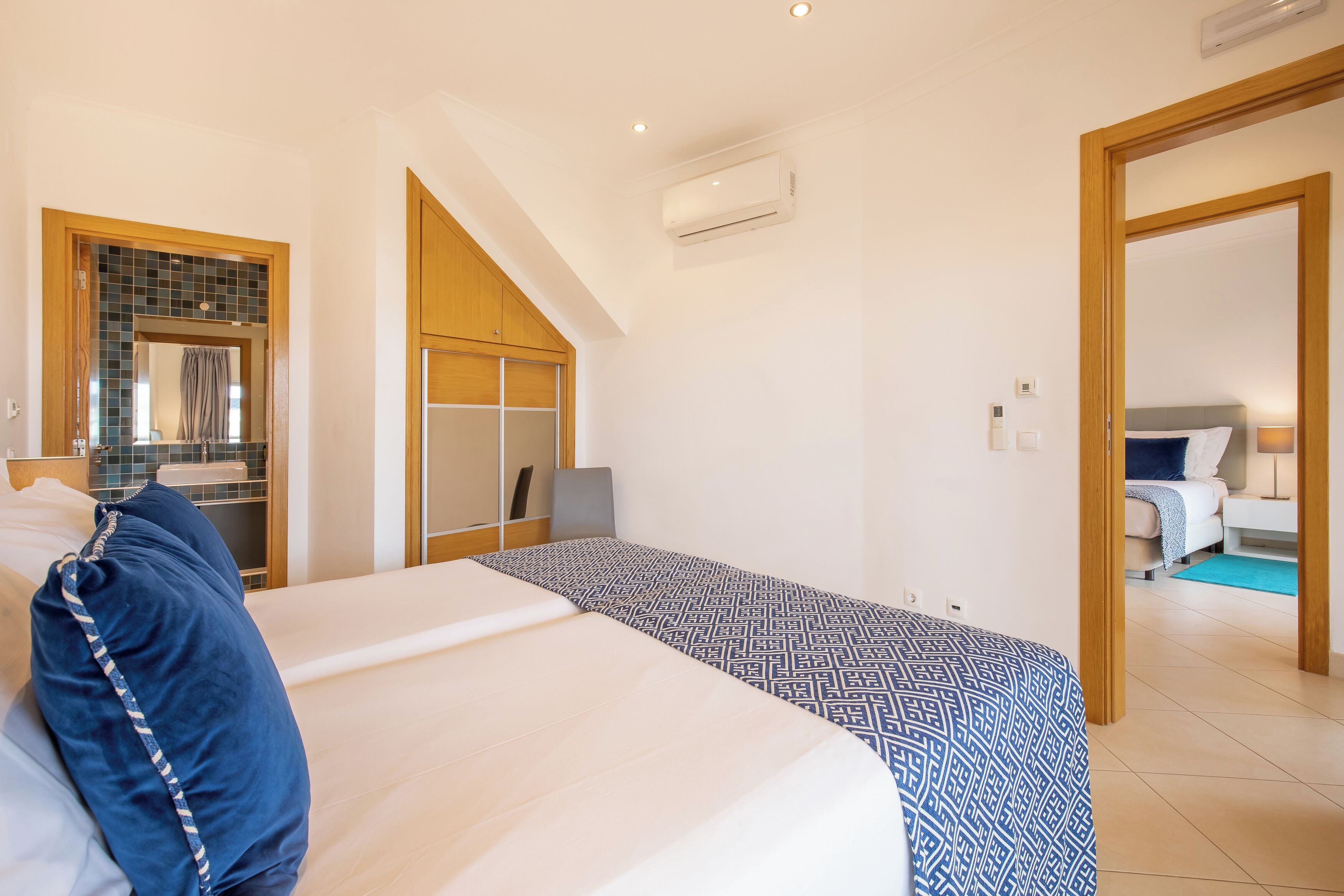A modern hotel room with a large bed, a wardrobe, a mirror, and a bathroom visible through an open door.