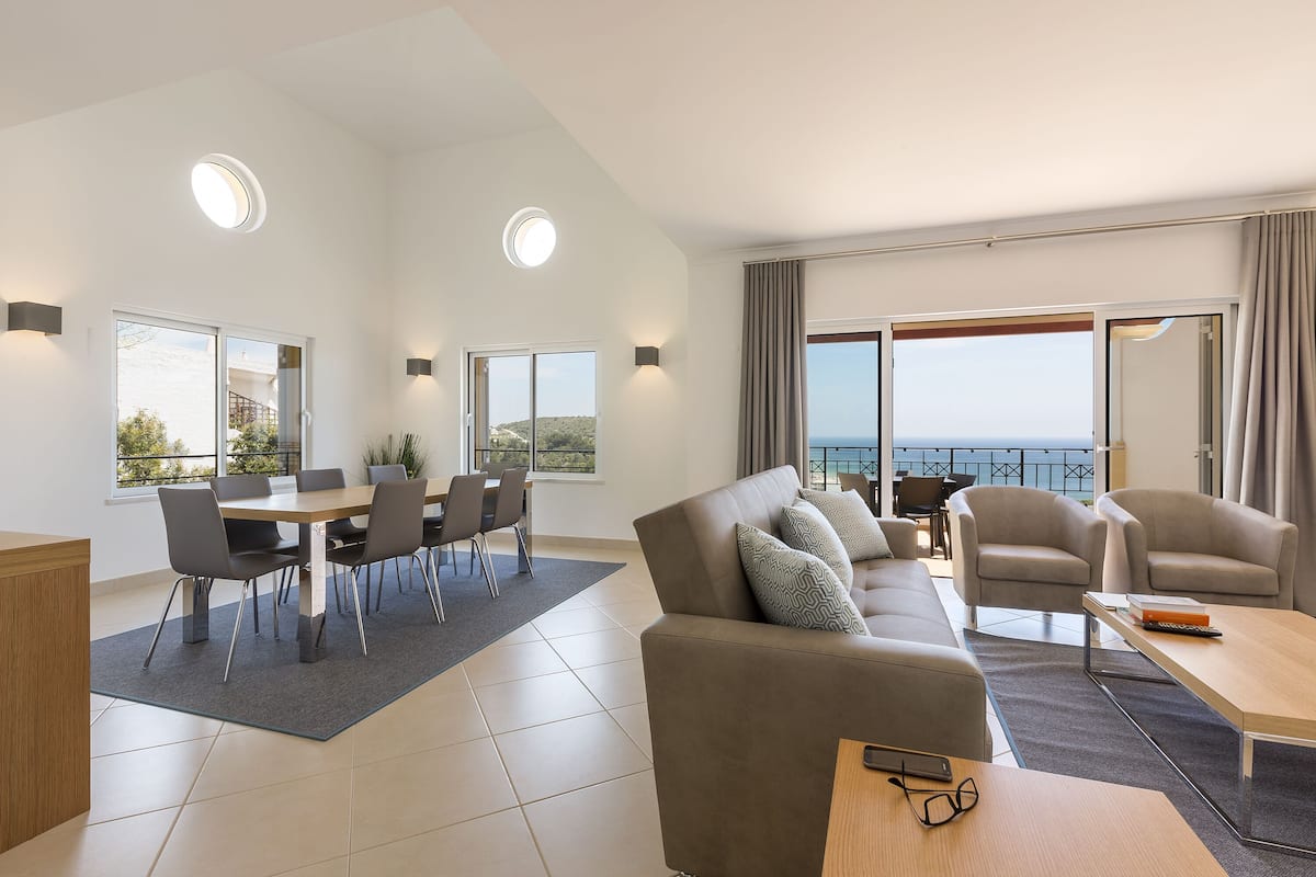 Ein modernes Wohnzimmer mit einer Couch, Sesseln, einem Esstisch und Meerblick.