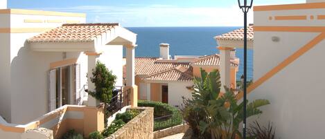 A coastal building with a paved courtyard, stone walls, and a view of the sea.
