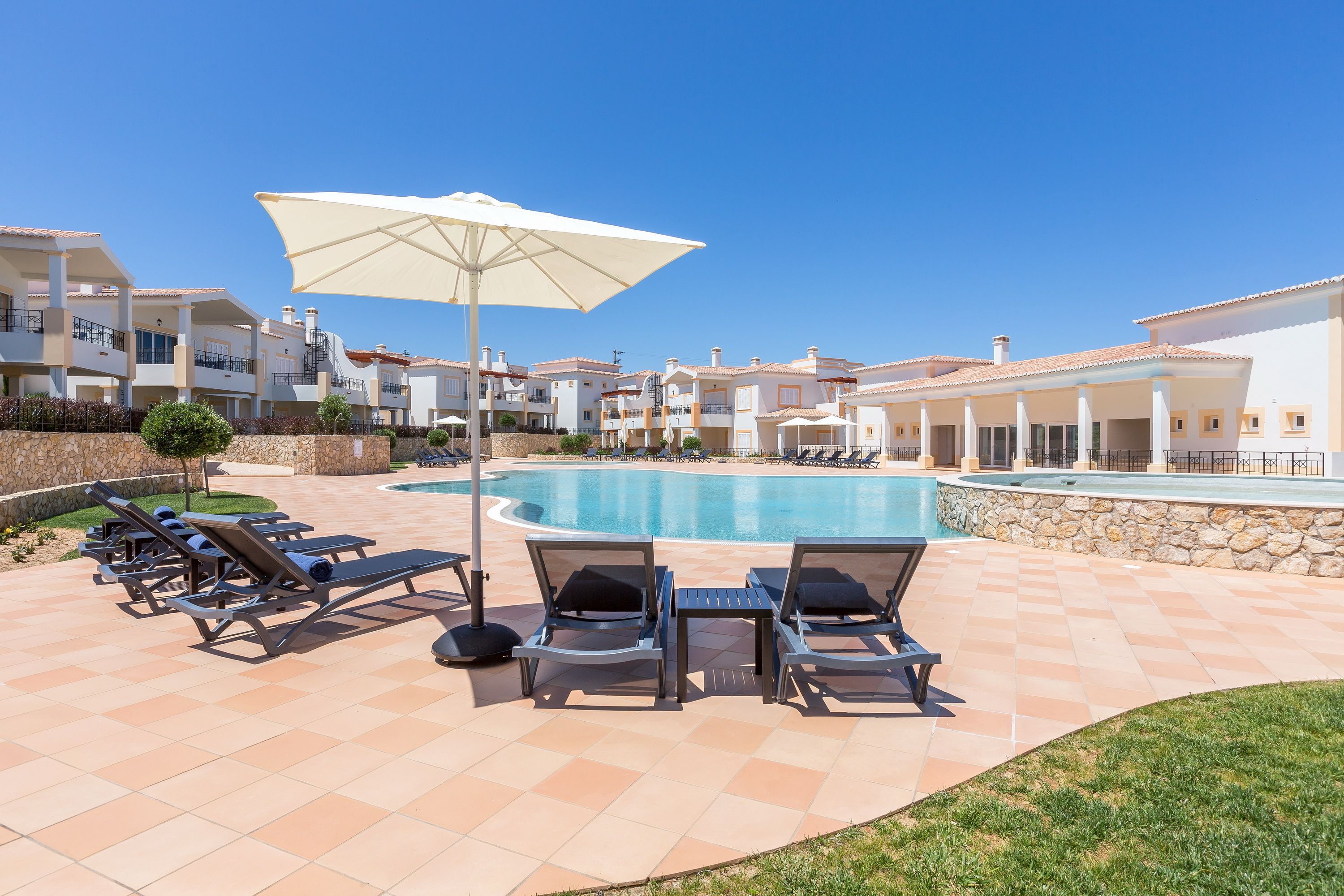 A pool area with lounge chairs and umbrellas, surrounded by modern buildings with balconies.