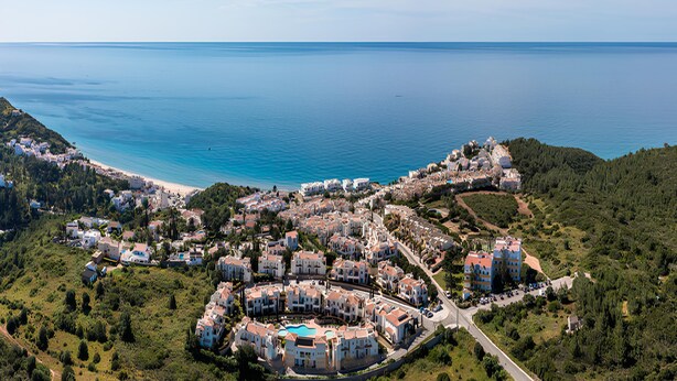Ein Küstenresort mit mehreren Gebäuden, einem Strand und freiem Blick auf das Meer.