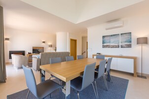 A modern living room with a wooden dining table, blue chairs, a sofa, and a fireplace.