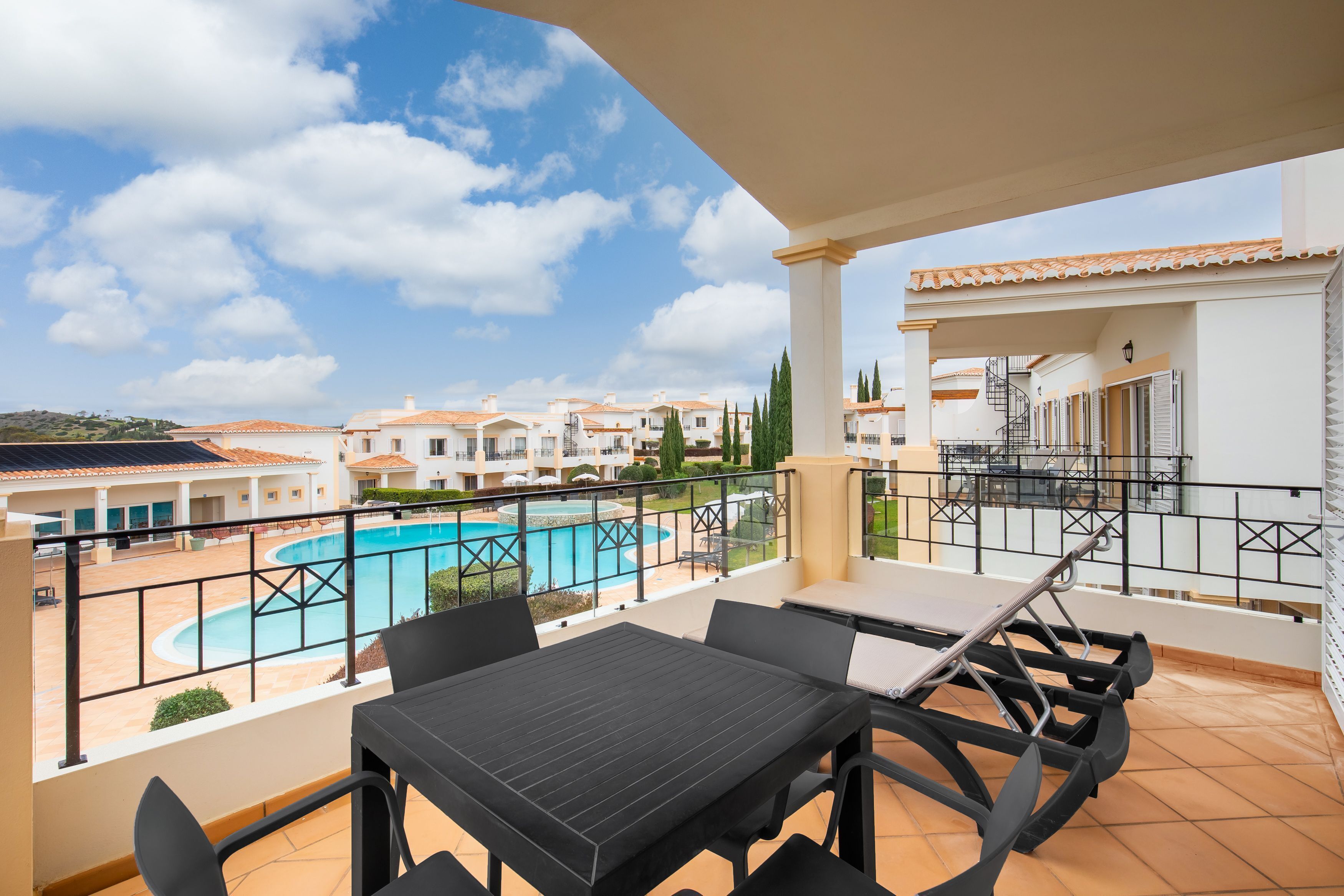 Un balcón con mesa y sillas que da a una piscina y una zona residencial.