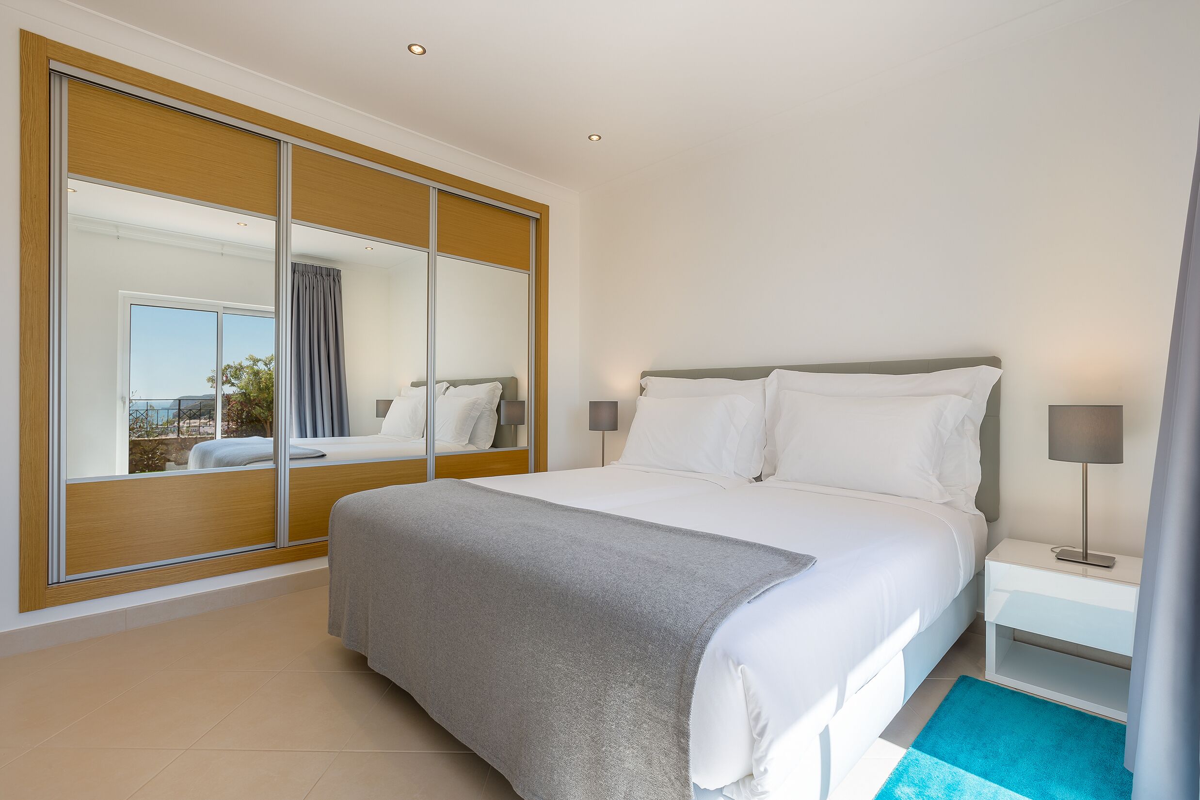 A modern hotel room with a large bed, a nightstand, a mirror, and a view of the outdoors.