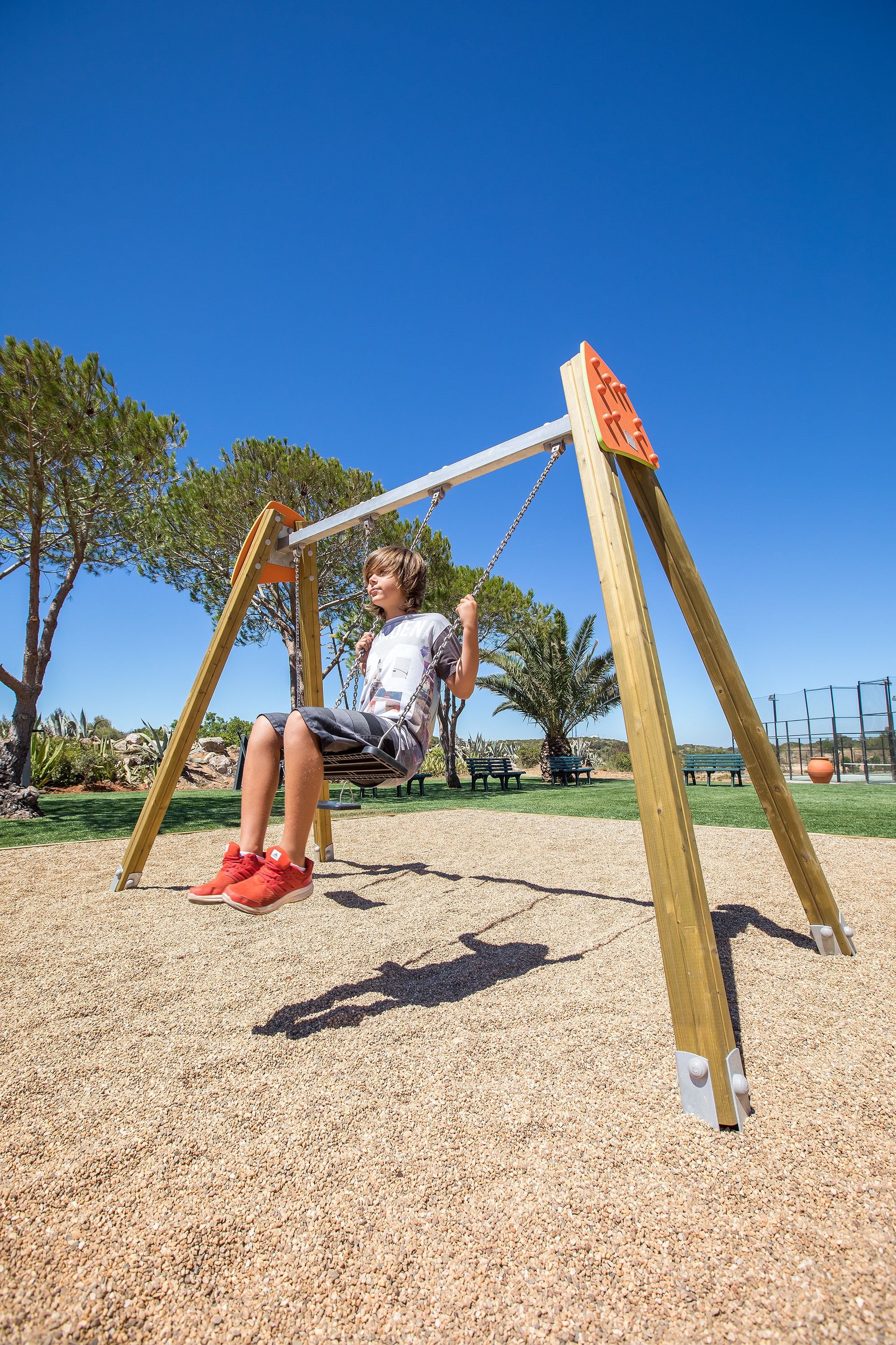 A child on a swing in a park with trees and a clear sky.