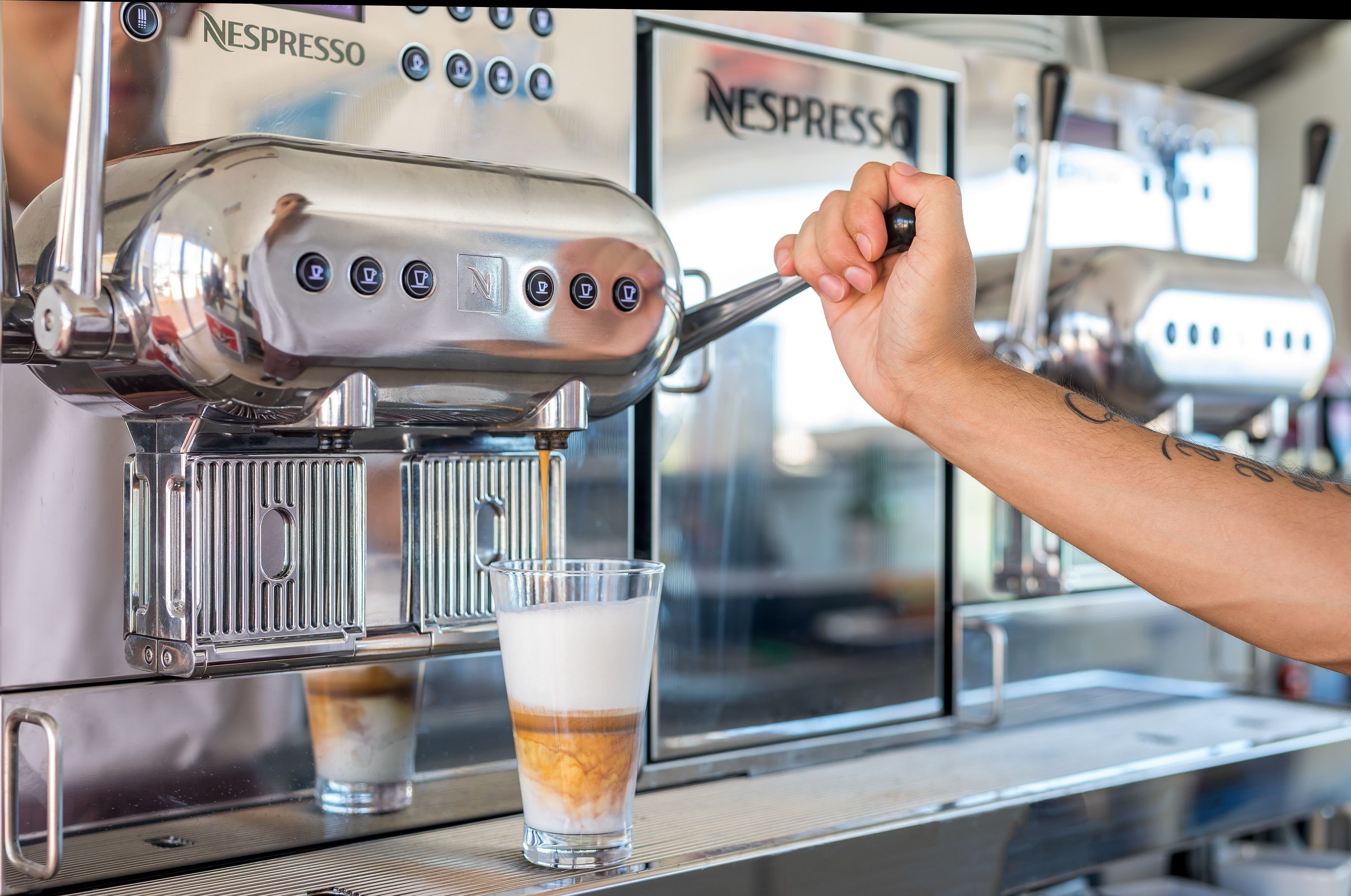 Une main actionne une machine à café Nespresso et verse le café dans un verre.