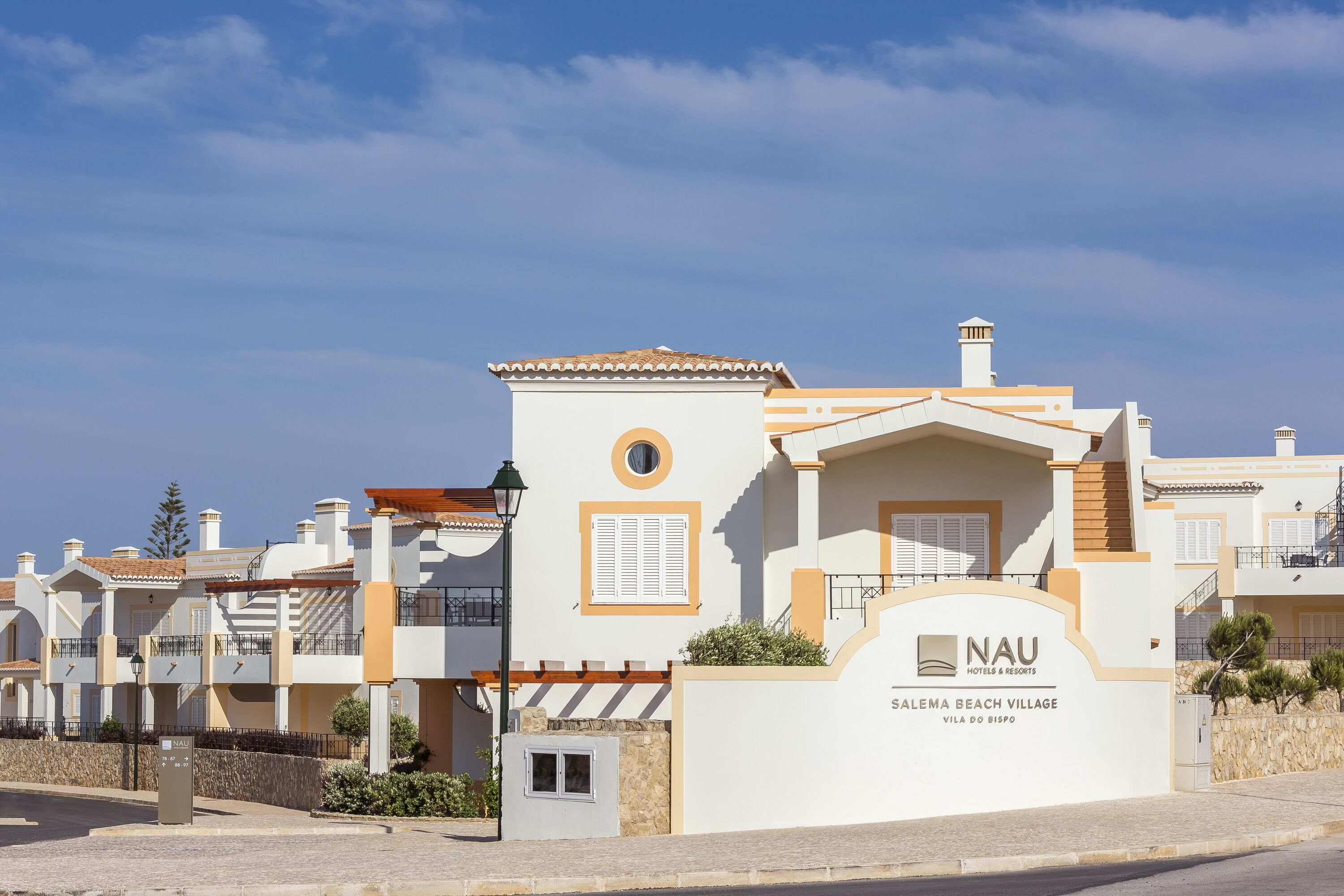 A modern hotel with a white facade, a sign reading "NAU Hotels & Resorts," and a view of the beach.
