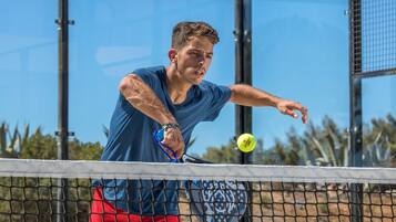 Un joueur de tennis en pleine action sur un court, avec un ciel dégagé en arrière-plan.