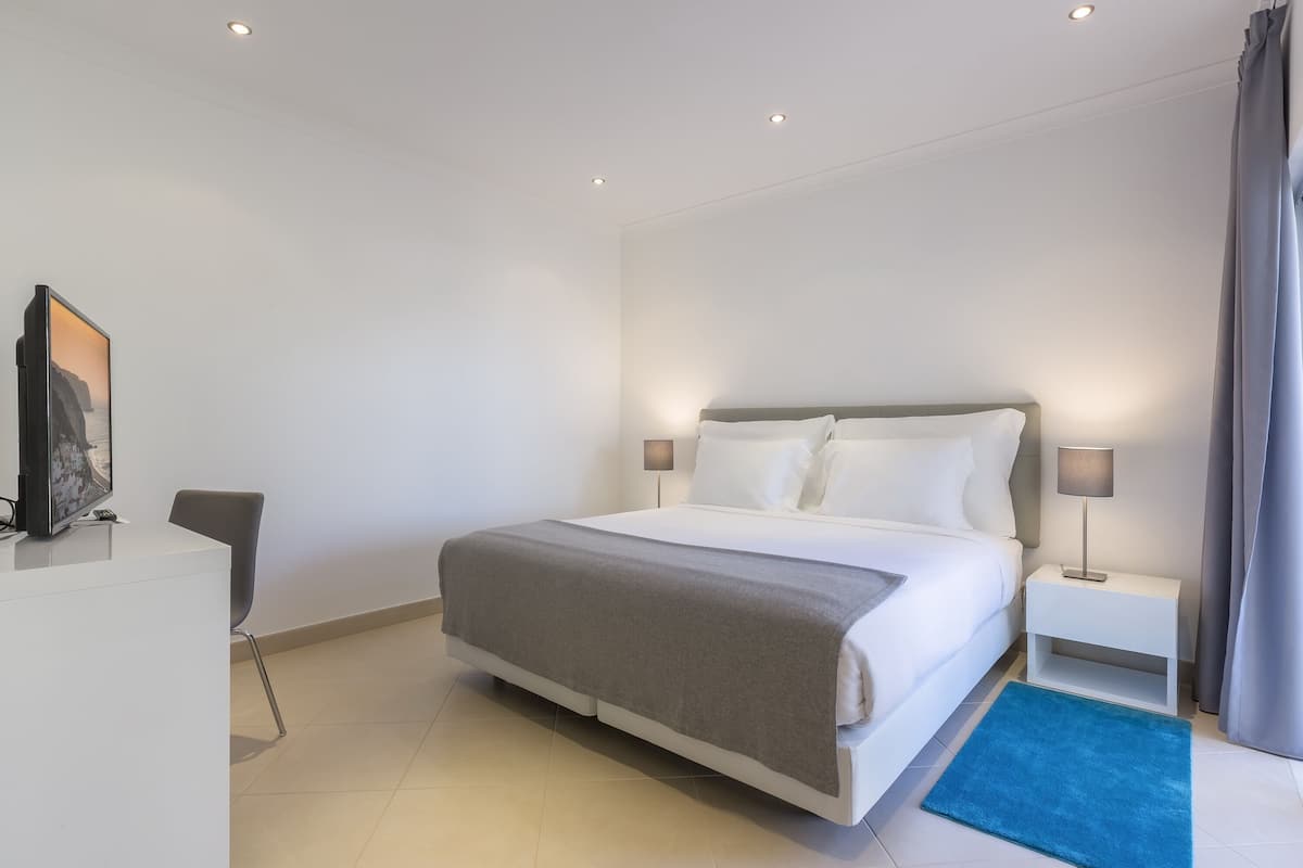 Ein modernes Hotelzimmer mit einem großen Bett, Nachttischen, einem Schreibtisch und einem Sessel.