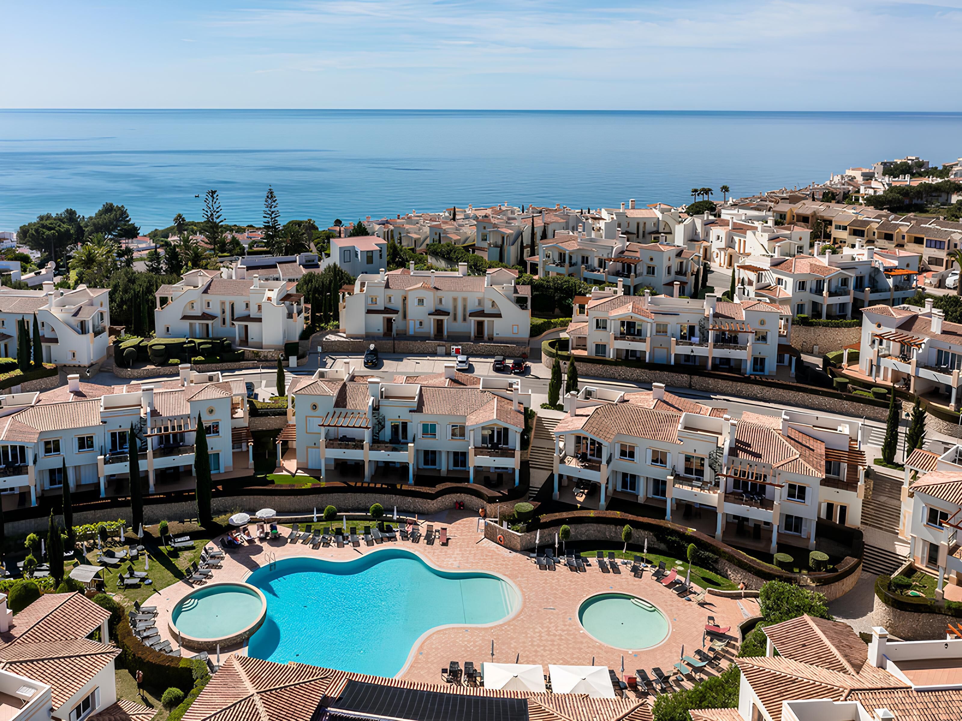 A coastal residential area with a large swimming pool surrounded by lounge chairs and umbrellas.