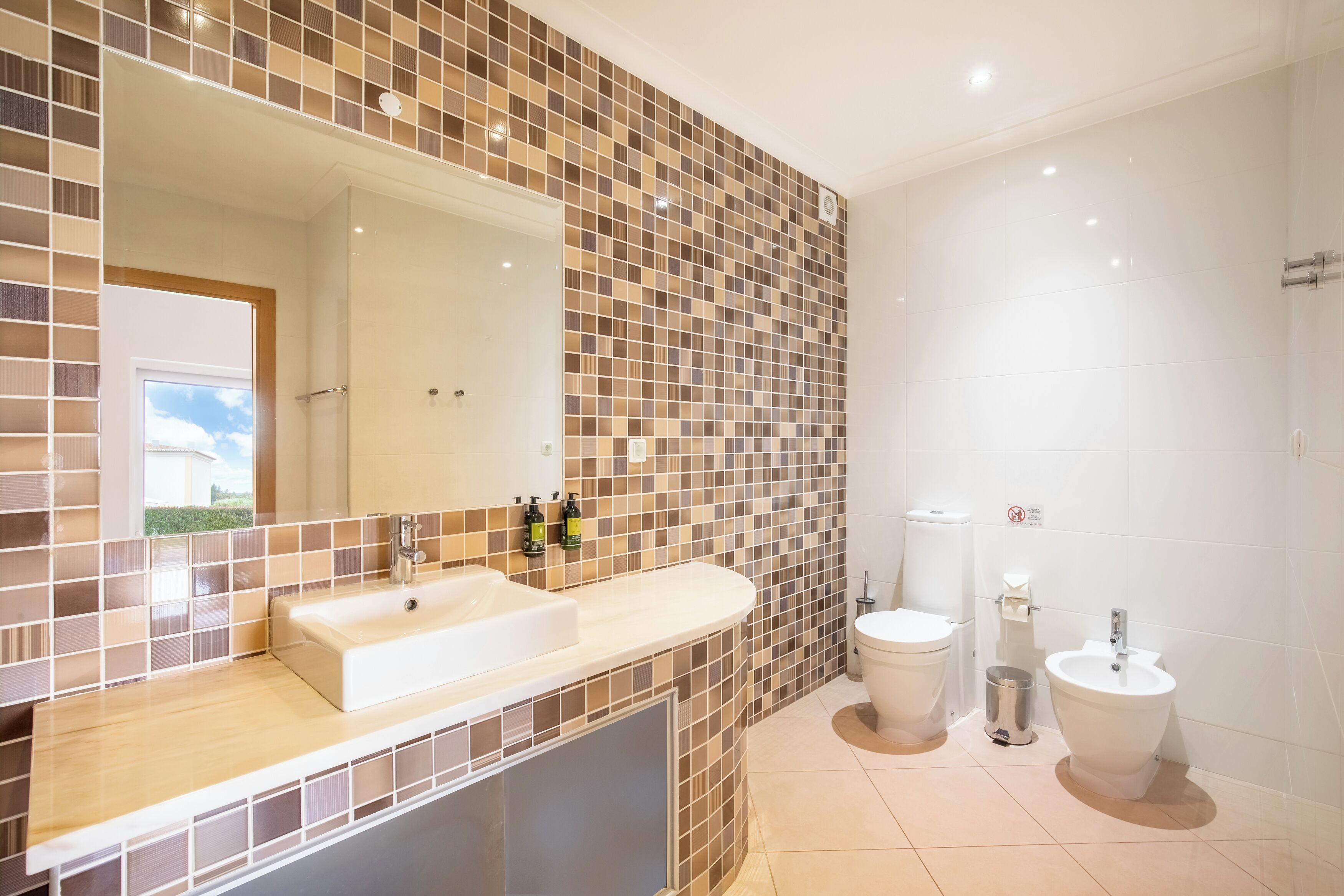 A bathroom with a large mirror, two sinks, a toilet, and a bidet.