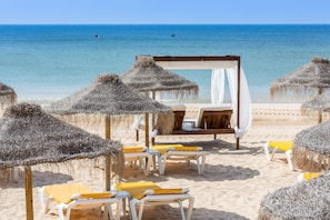 Une plage avec des parasols en chaume, des chaises longues et une structure en forme de tonnelle.