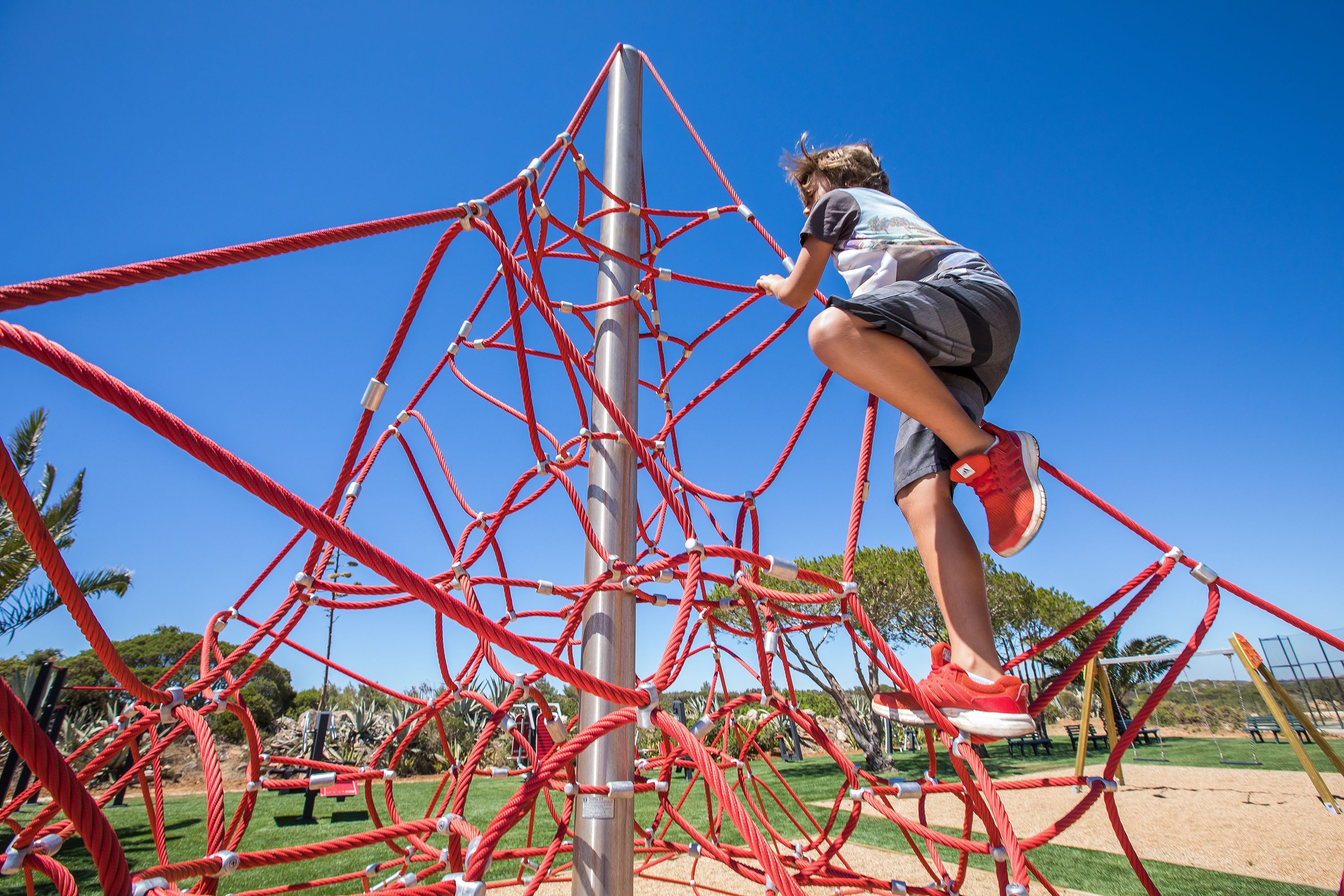 A child climbing a red rope structure at a playground.
