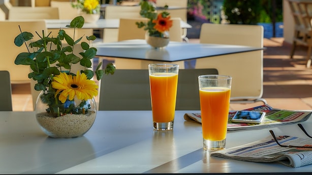 Ein Tisch mit zwei Gläsern Orangensaft, einer Vase mit gelben Blumen und einer Zeitung.