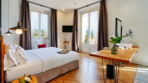 Ein Hotelzimmer mit einem großen Bett, einem Holztisch, einem Fernseher und Blick ins Freie.