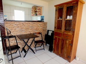 A kitchen with a stone backsplash, a wooden cabinet, and a dining table with chairs. - Sol de Geribá (Búzios)