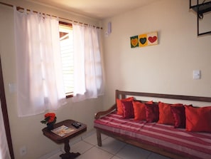 A room with a bed, a small table with a magazine, and a window with white curtains. - Sol de Geribá (Búzios)