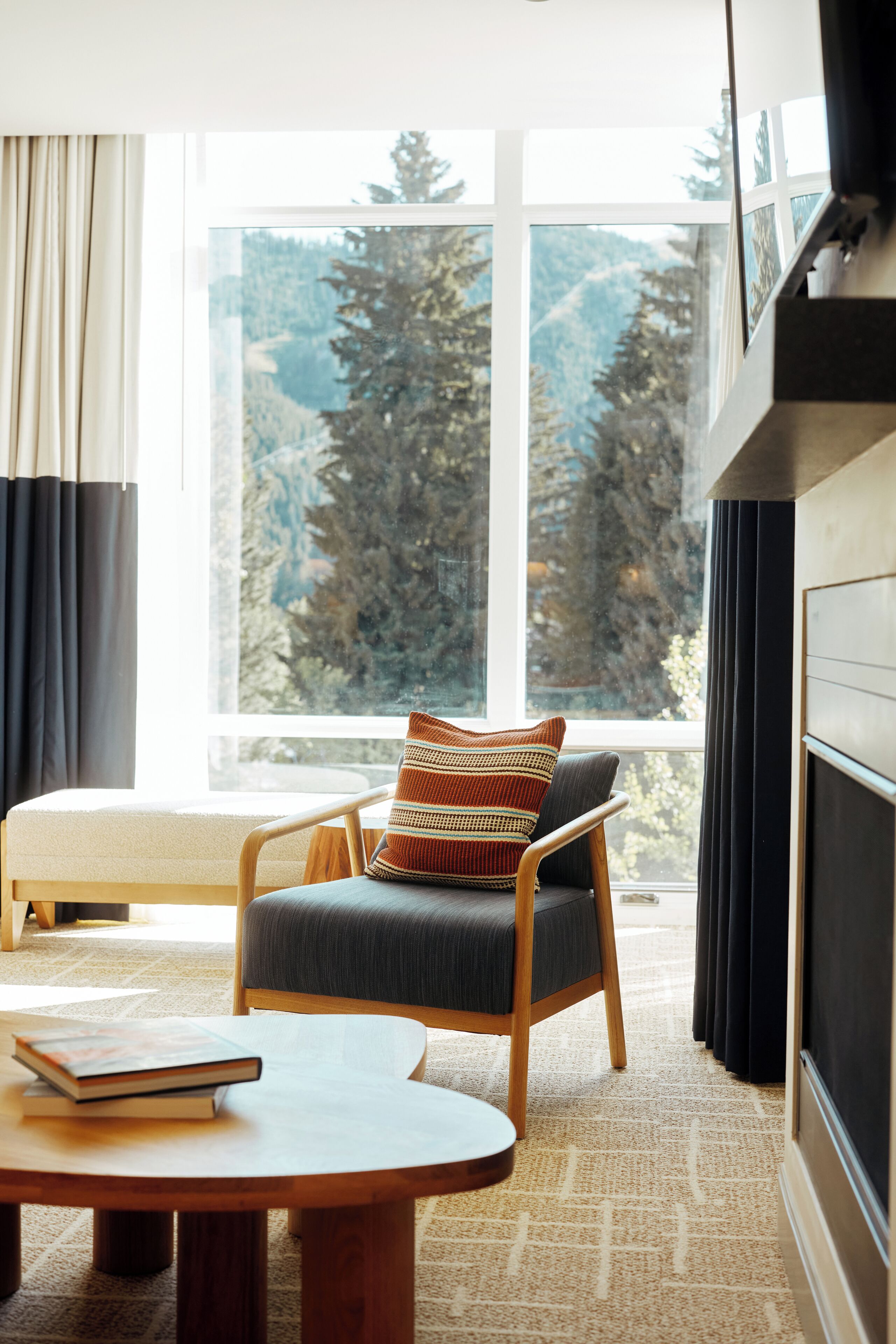 Ein Zimmer mit einem großen Fenster, einem Holzstuhl mit Kissen, einem kleinen Rundtisch und einem Buch.