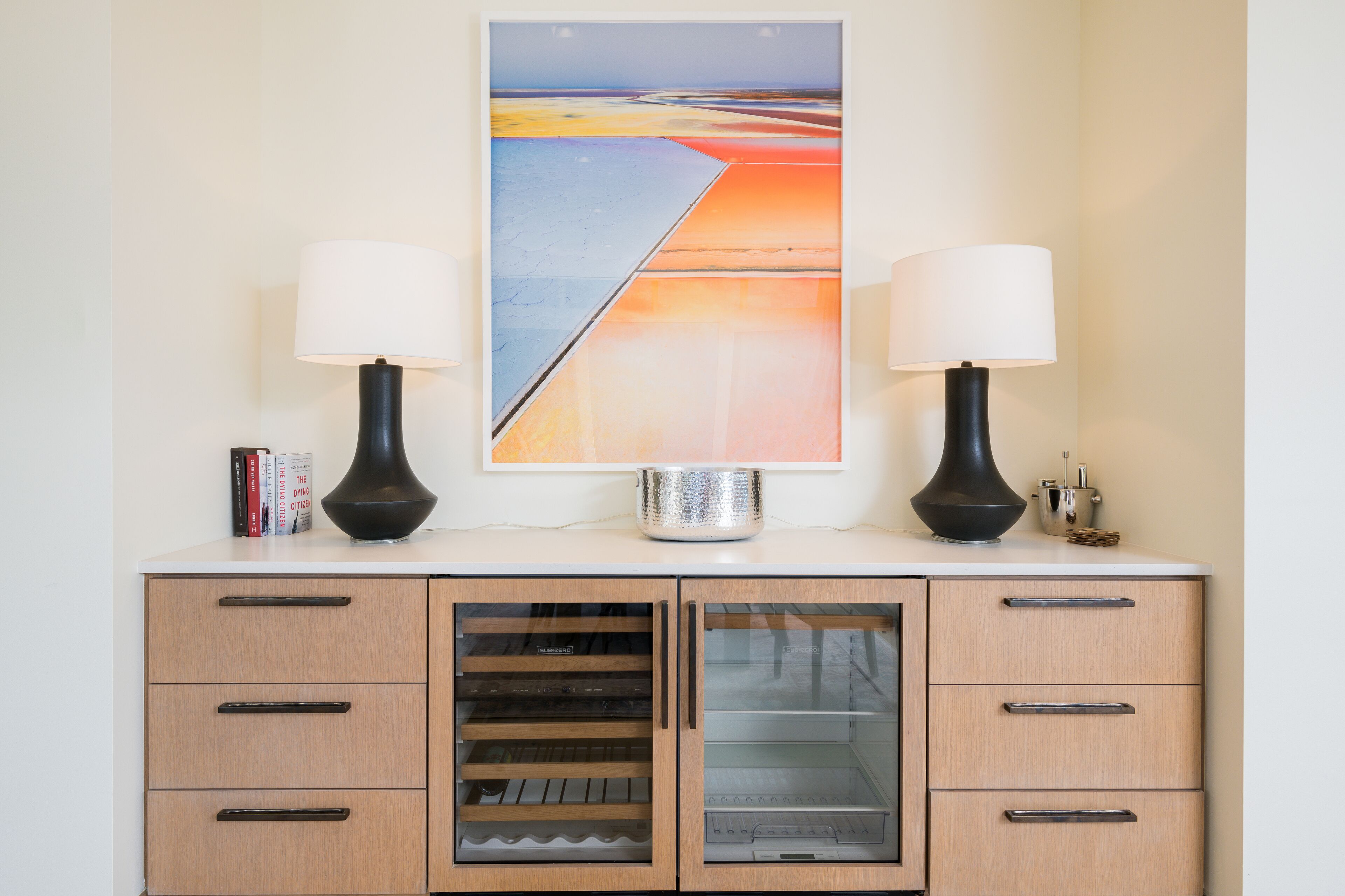 A modern kitchen with a built-in oven, a refrigerator, and a countertop with two lamps and a decorative item.