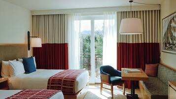 A hotel room with a bed, a sofa, a table with a lamp, and a view of the outdoors through a large window.