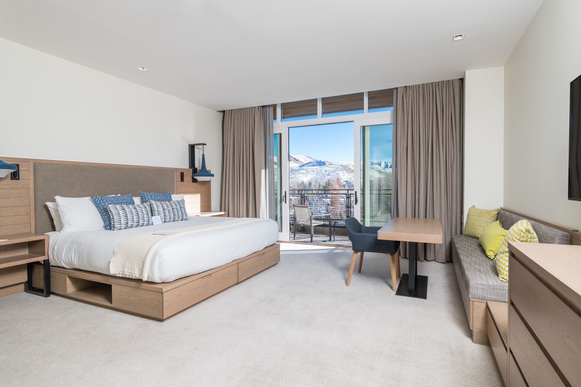 Et moderne hotelværelse med en stor seng, et skrivebord og en balkon med udsigt til bjerge.
