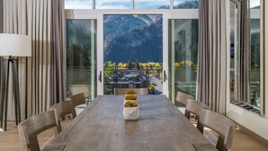 A dining area with a large table, chairs, and a view of mountains through large windows. - Limelight Hotel Ketchum (Ketchum)