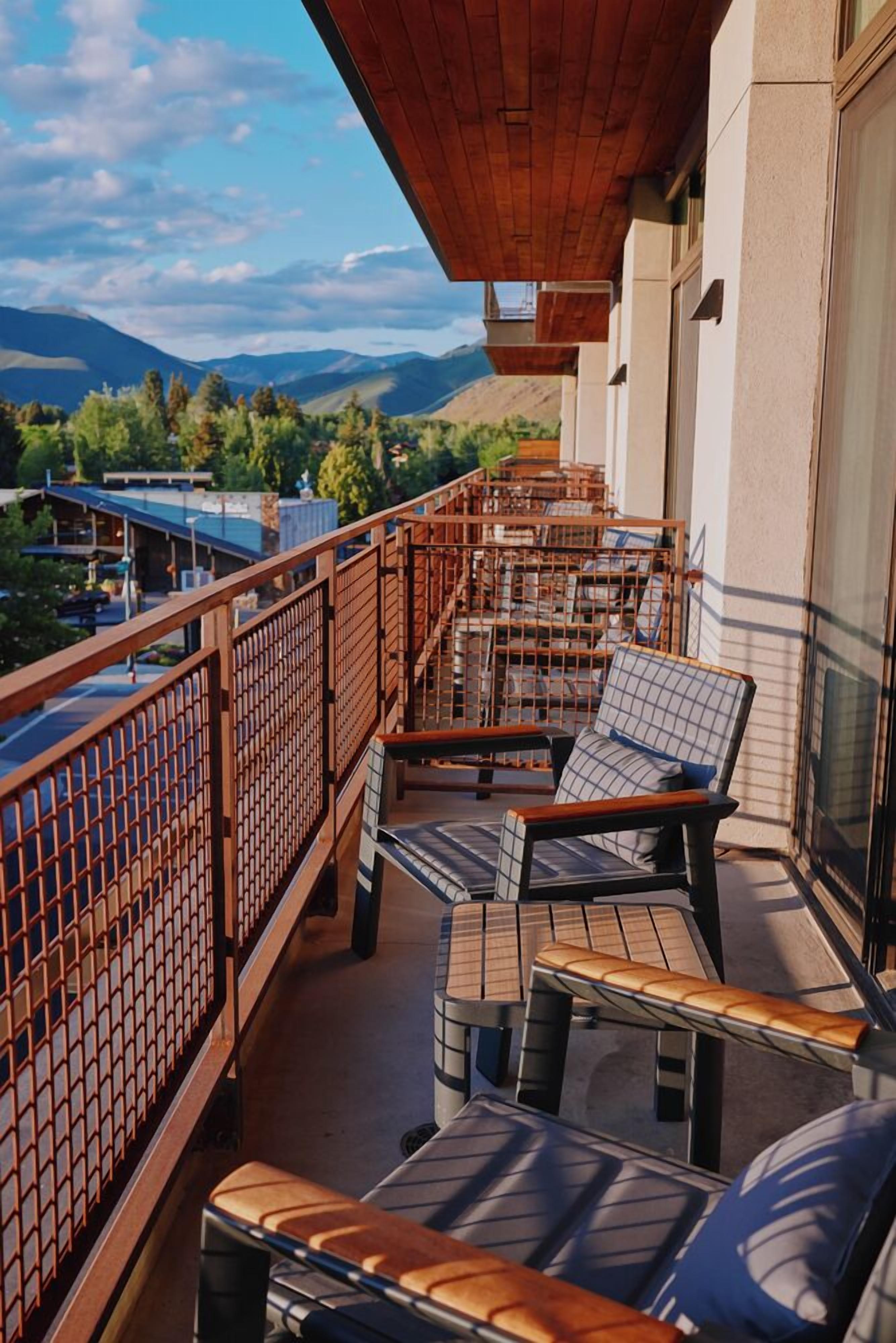 A balcony with wooden railings, a table, and two cushioned chairs with patterned cushions.