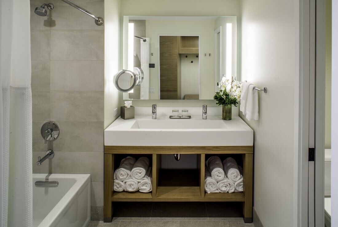 Un baño moderno con un lavamanos blanco, un espejo y dos toalleros. Cuenta con una zona de ducha con puerta de cristal y una bañera.