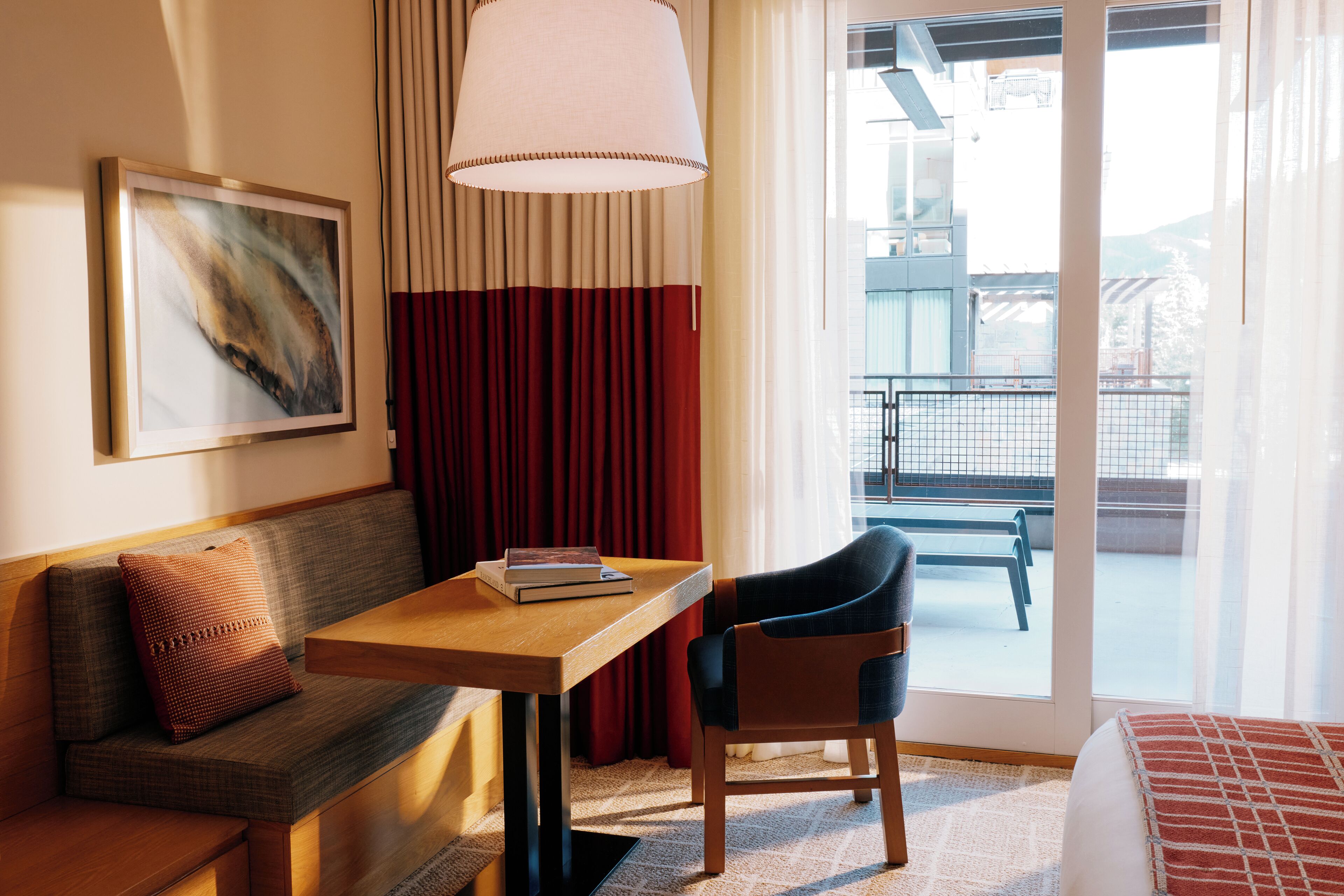 Habitación de hotel con sofá, una mesita con un libro, una silla, un ventanal grande y un cuadro en la pared.