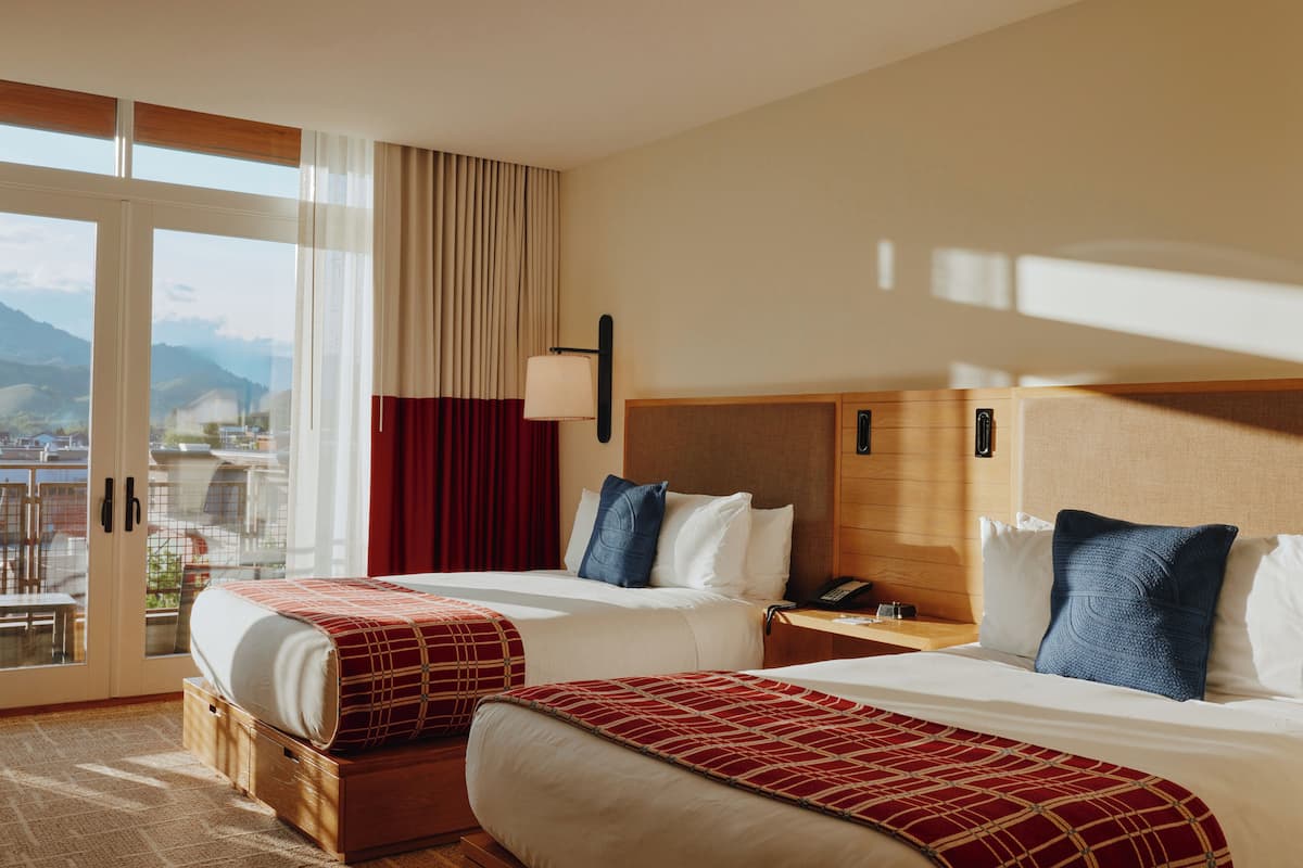 Une chambre d’hôtel avec deux lits, une grande fenêtre donnant sur les montagnes et une tête de lit en bois.