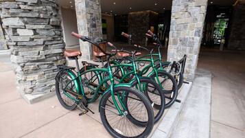 Uma fileira de bicicletas verdes estacionadas em frente a um pilar de pedra em um espaço interno bem iluminado, com parede de pedra e um banco de madeira.
