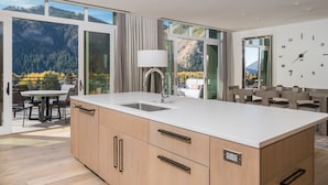 Une cuisine moderne dotée d’un grand îlot central, de meubles en bois et offrant une vue sur un paysage montagneux grâce à de grandes fenêtres.