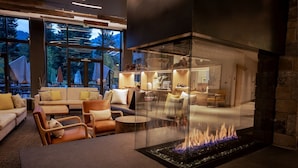 A modern living room with a glass fireplace, comfortable seating, and large windows offering a view of the outdoors. - Limelight Hotel Ketchum (Ketchum)