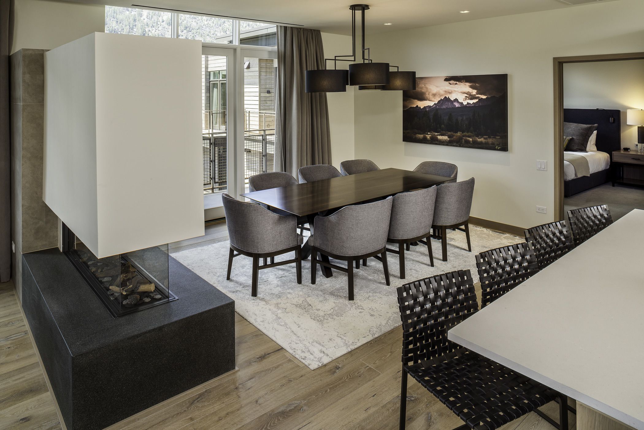 A modern hotel room with a dining area, a fireplace, and a large window with a view.