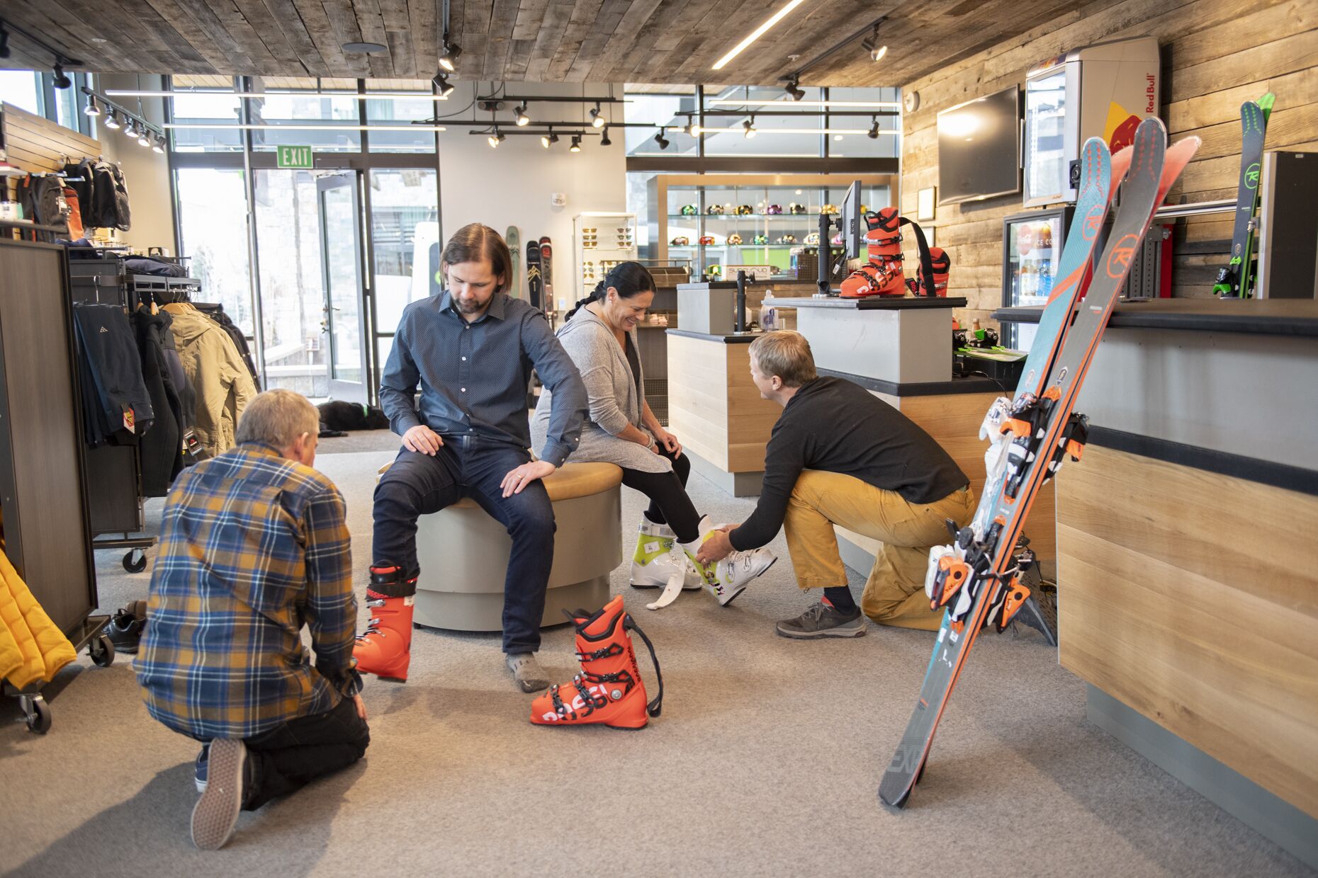 Un magasin de location de skis, avec un intérieur en bois, un comptoir où sont exposés les équipements de ski, et un grand ski appuyé contre le mur.