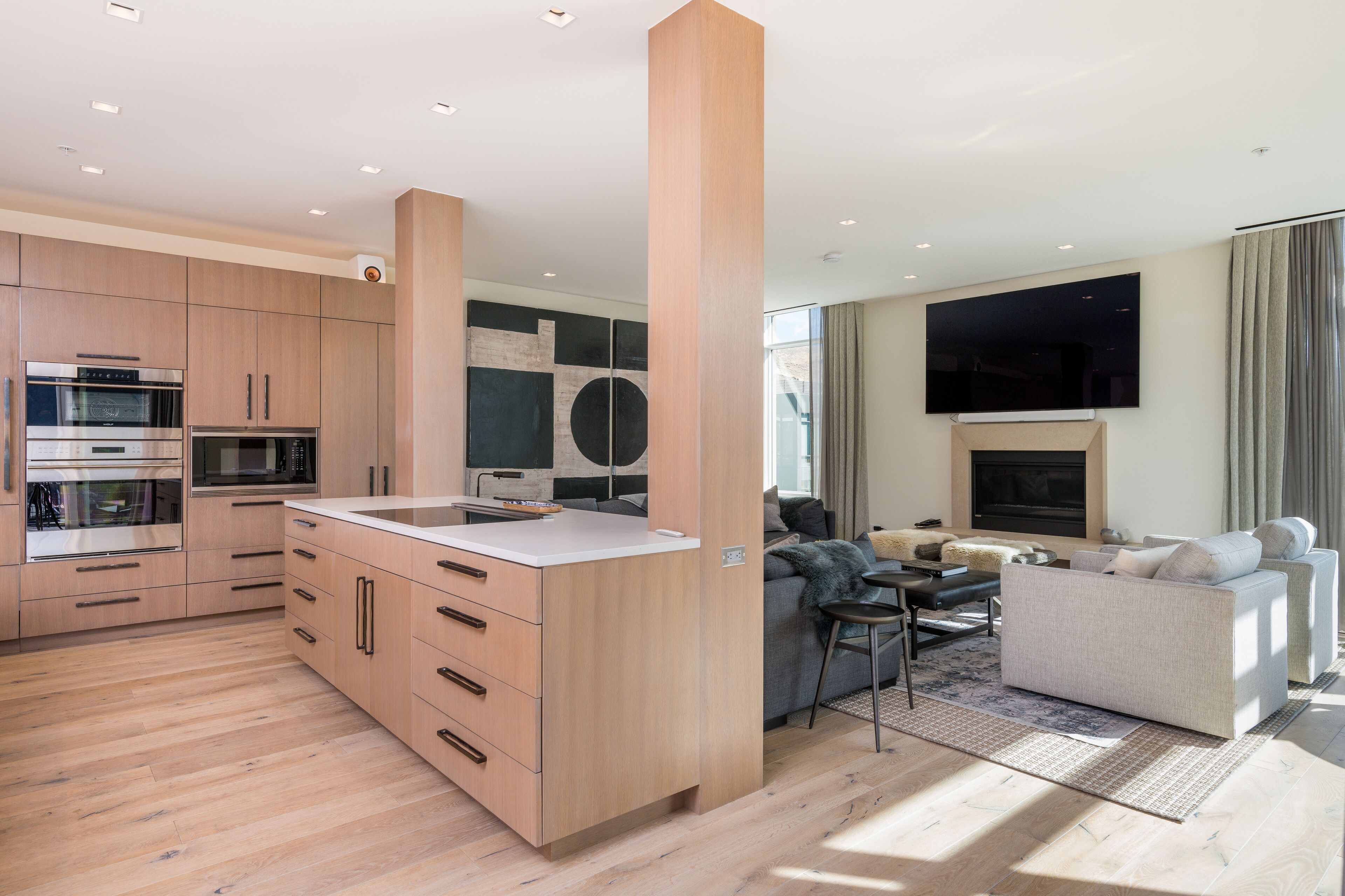 A modern kitchen with built-in appliances, a dining area with a sofa and a TV, and a living room with a fireplace.