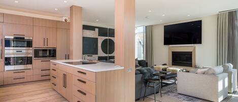 A modern kitchen with built-in appliances, a dining area with a sofa and a TV, and a living room with a fireplace.