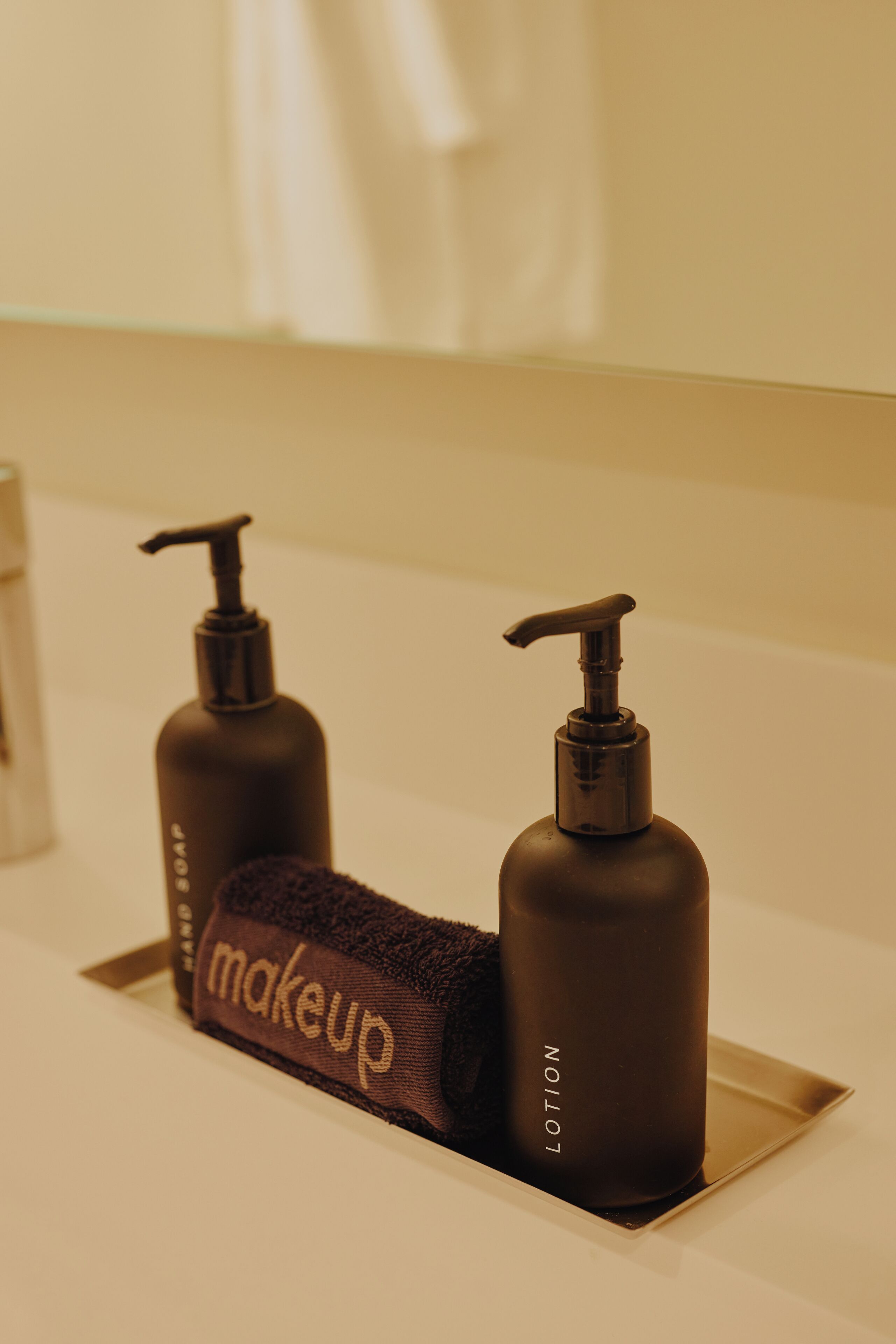 Een badkamer met twee donkere lotionflessen en een handdoek met de tekst 'makeup' op een witte wastafel.
