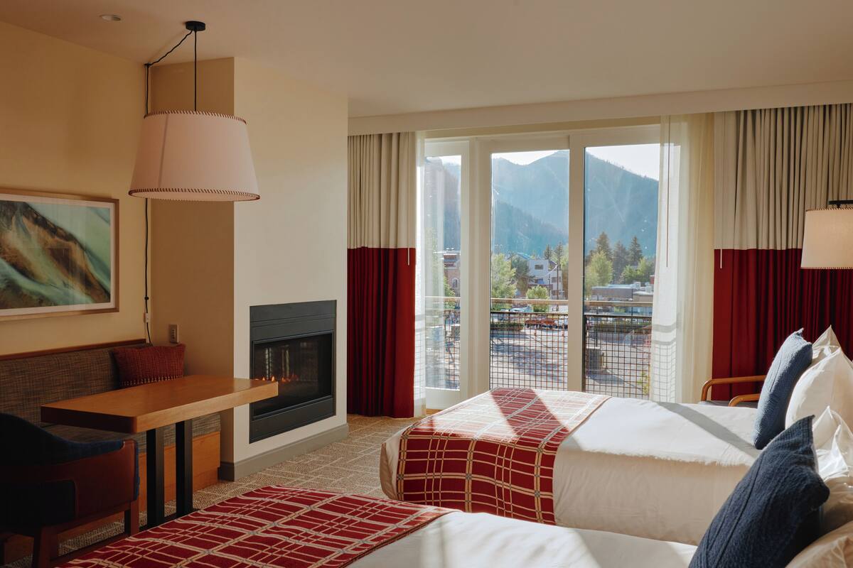 Une chambre d’hôtel comprenant un lit, un canapé, une table, une cheminée et une grande fenêtre donnant sur les montagnes.